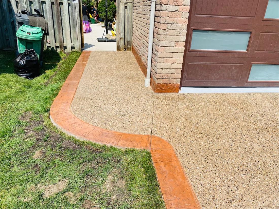 New exposed aggregate walkway with a red stamped border beside a lawn